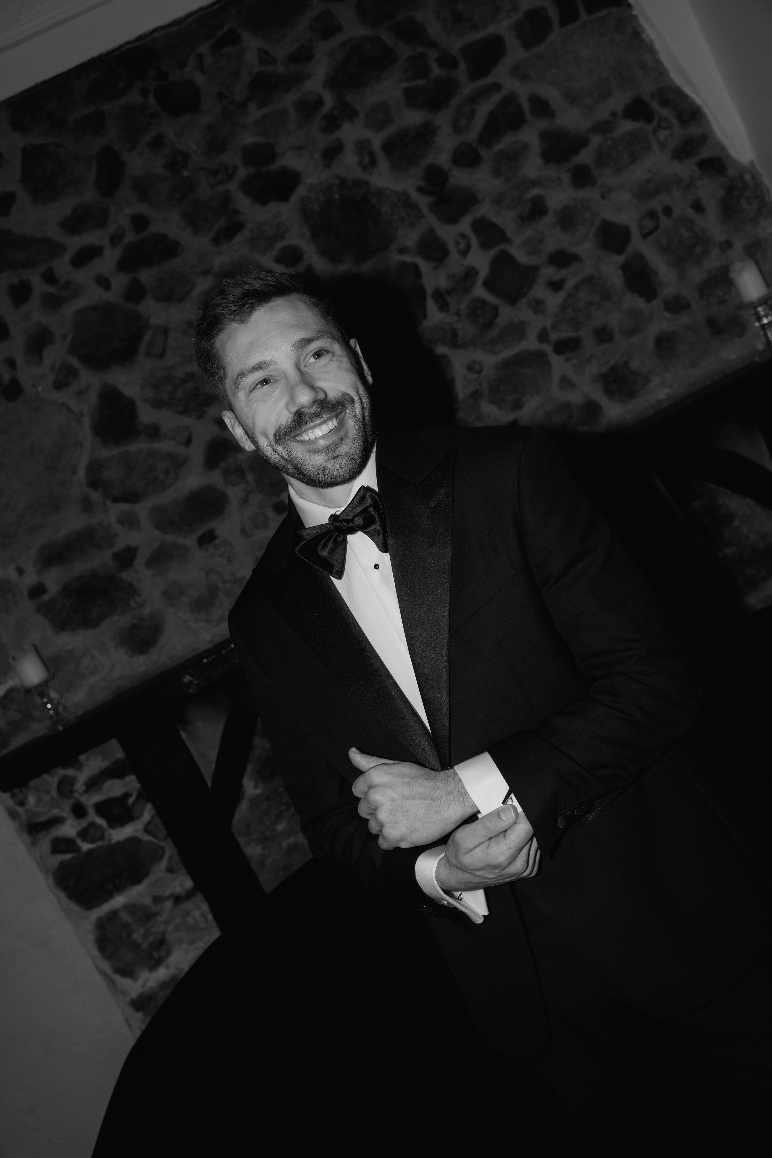 A black and white photograph showing someone in formal attire against a stone wall.