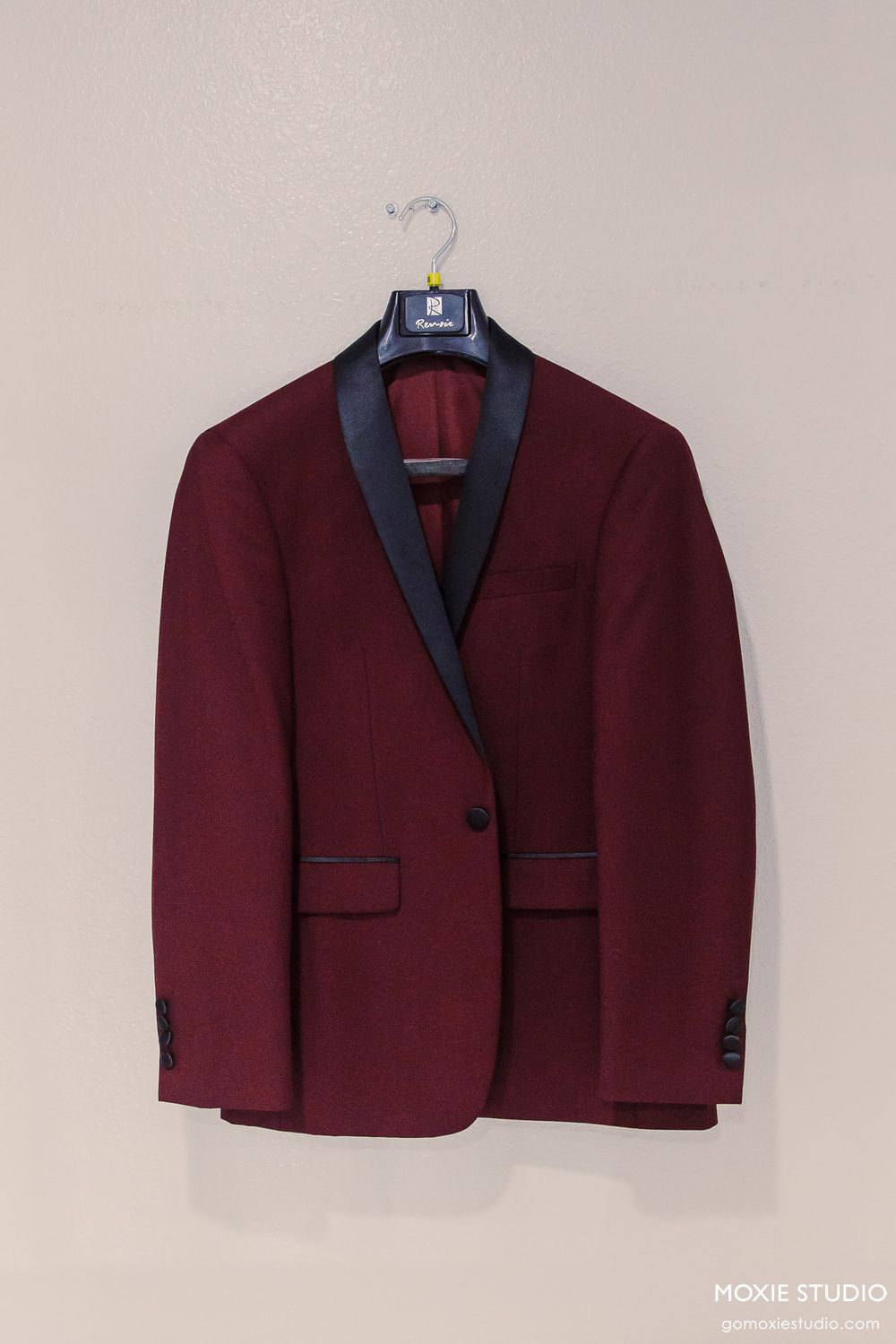Burgundy tuxedo jacket with black lapels displayed on a hanger against light background.