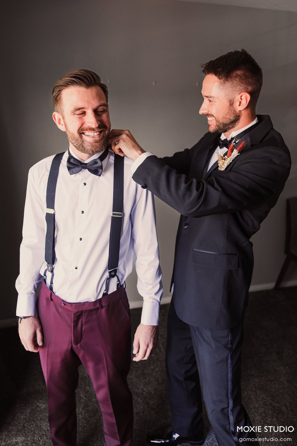 Two people in wedding attire share a candid moment while adjusting formal wear.