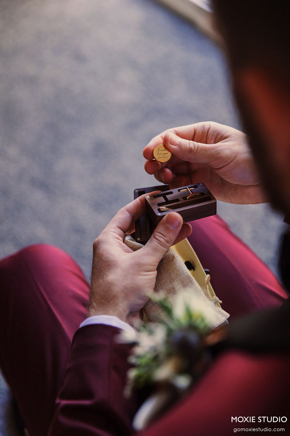 Close-up of hands holding a ring box while wearing burgundy formal pants.