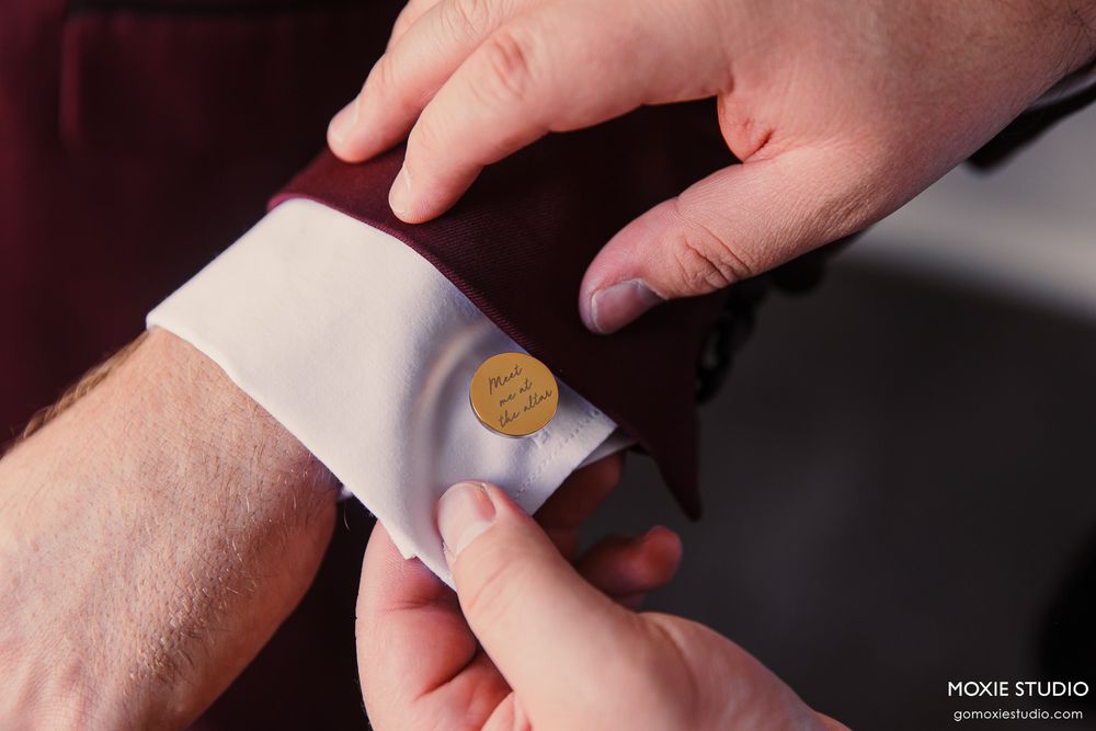 Detail shot of hands fastening a gold cufflink on a white dress shirt sleeve.