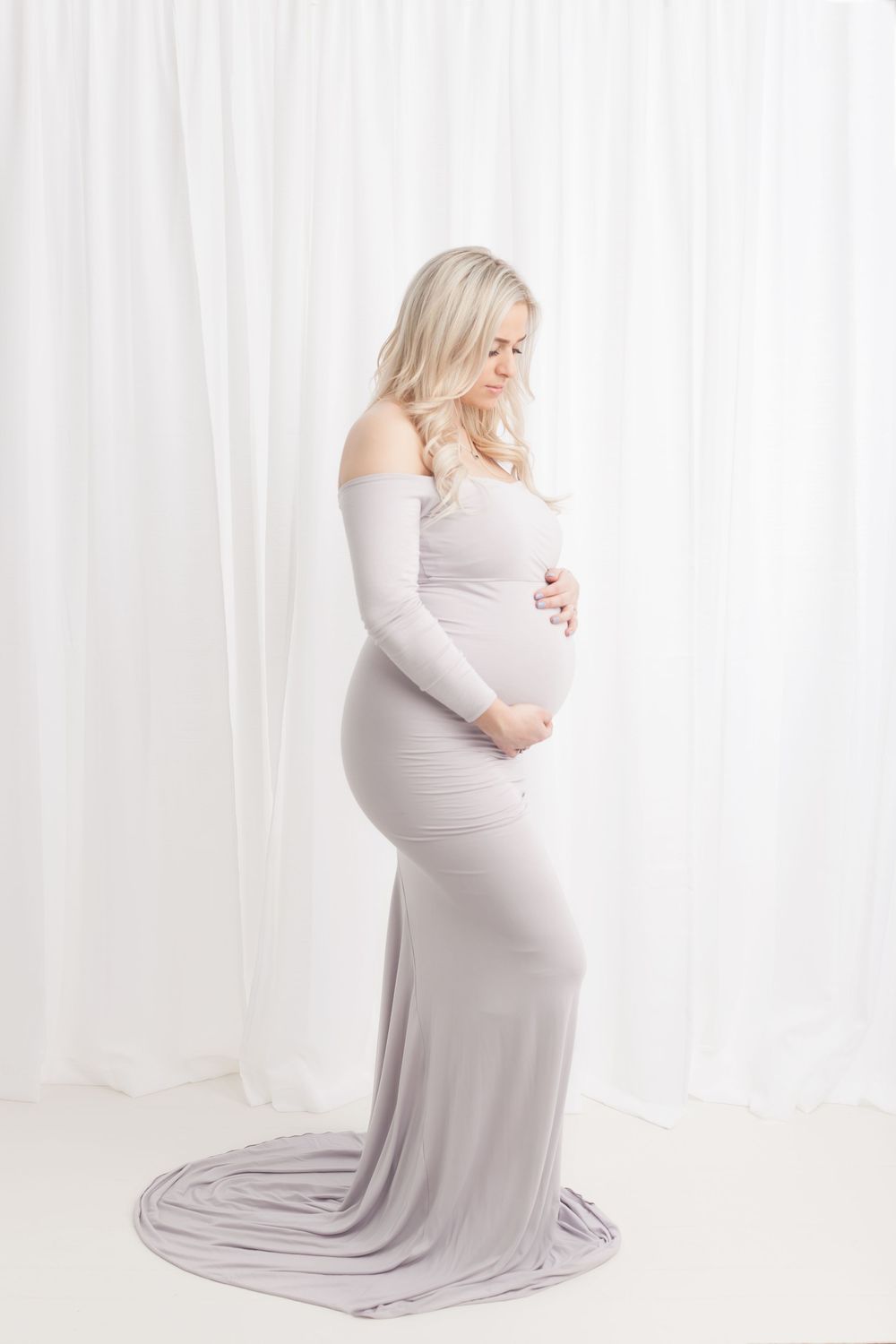 Four elegant maternity photos show a woman in a flowing gray gown against a white curtained backdrop.