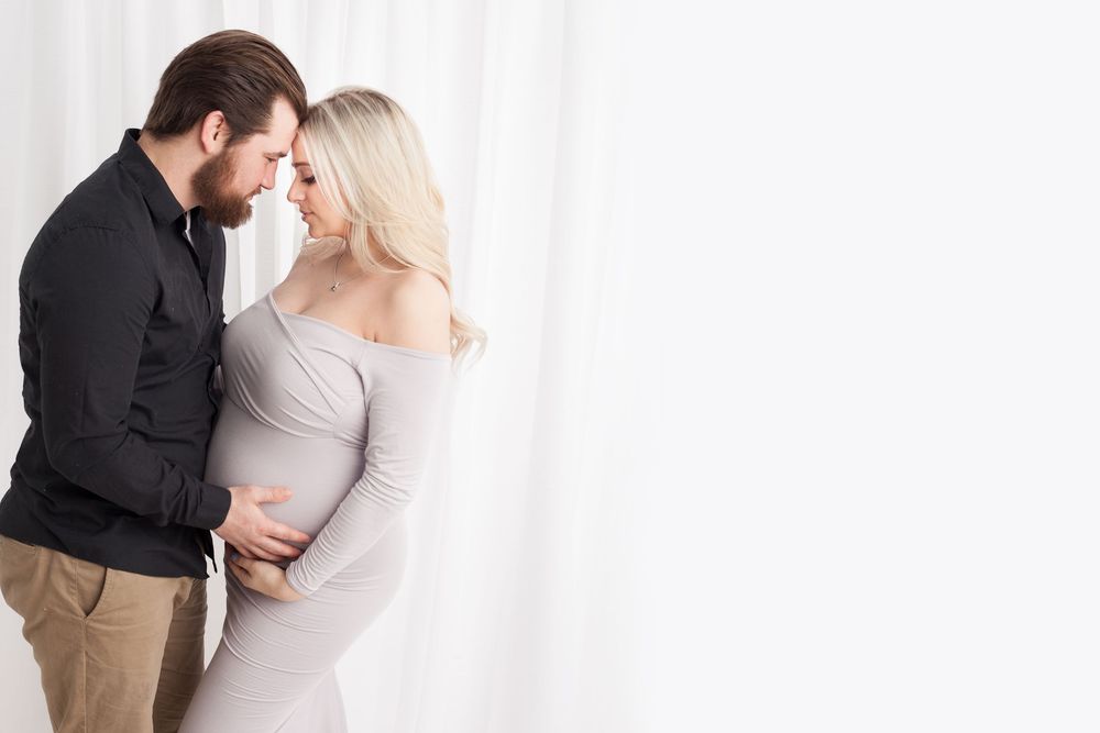 A couple stands close together against a white background while sharing a tender moment.