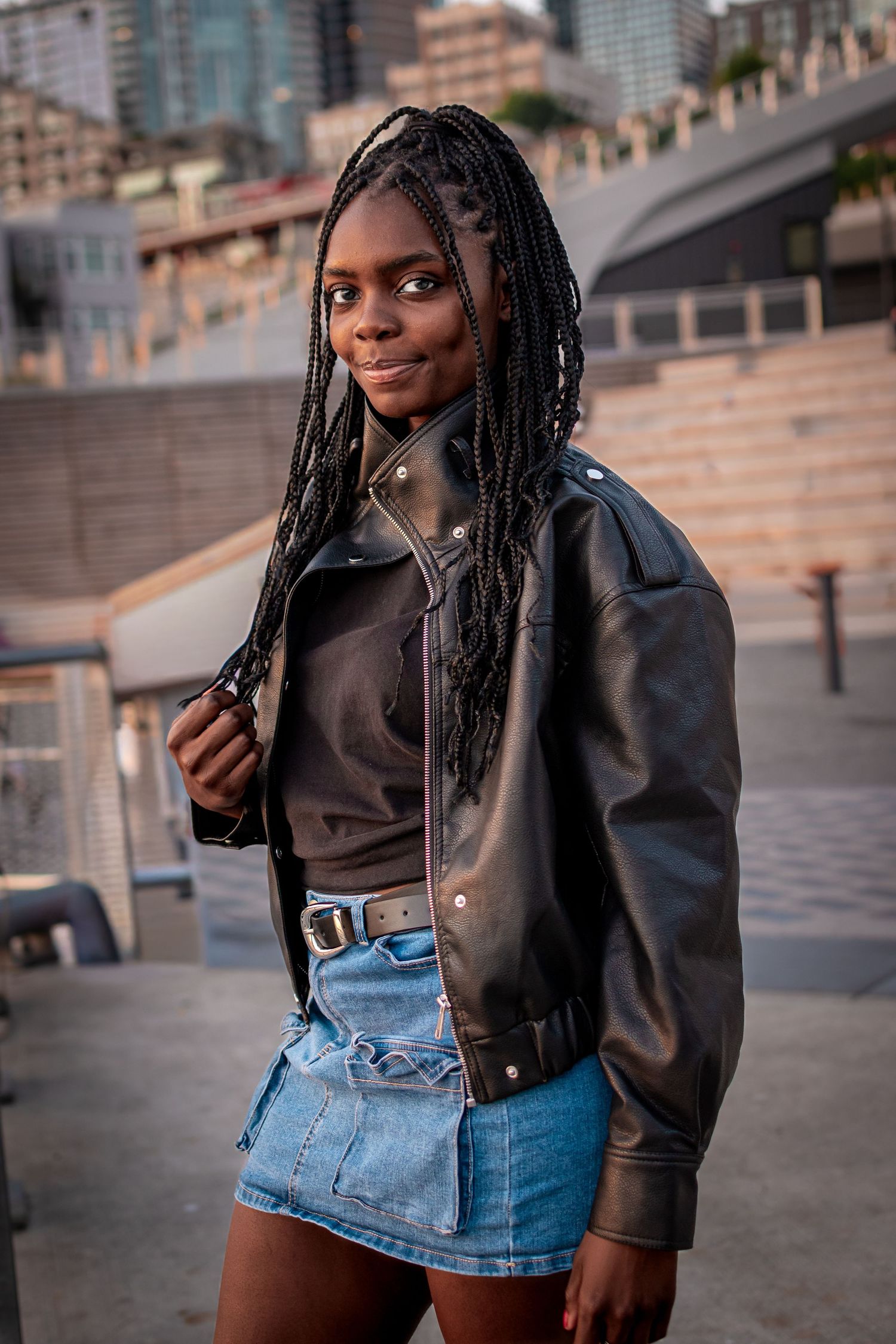 High school senior wearing a leather jacket and denim skirt in downtown Seattle with the waterfront skyline in the background.