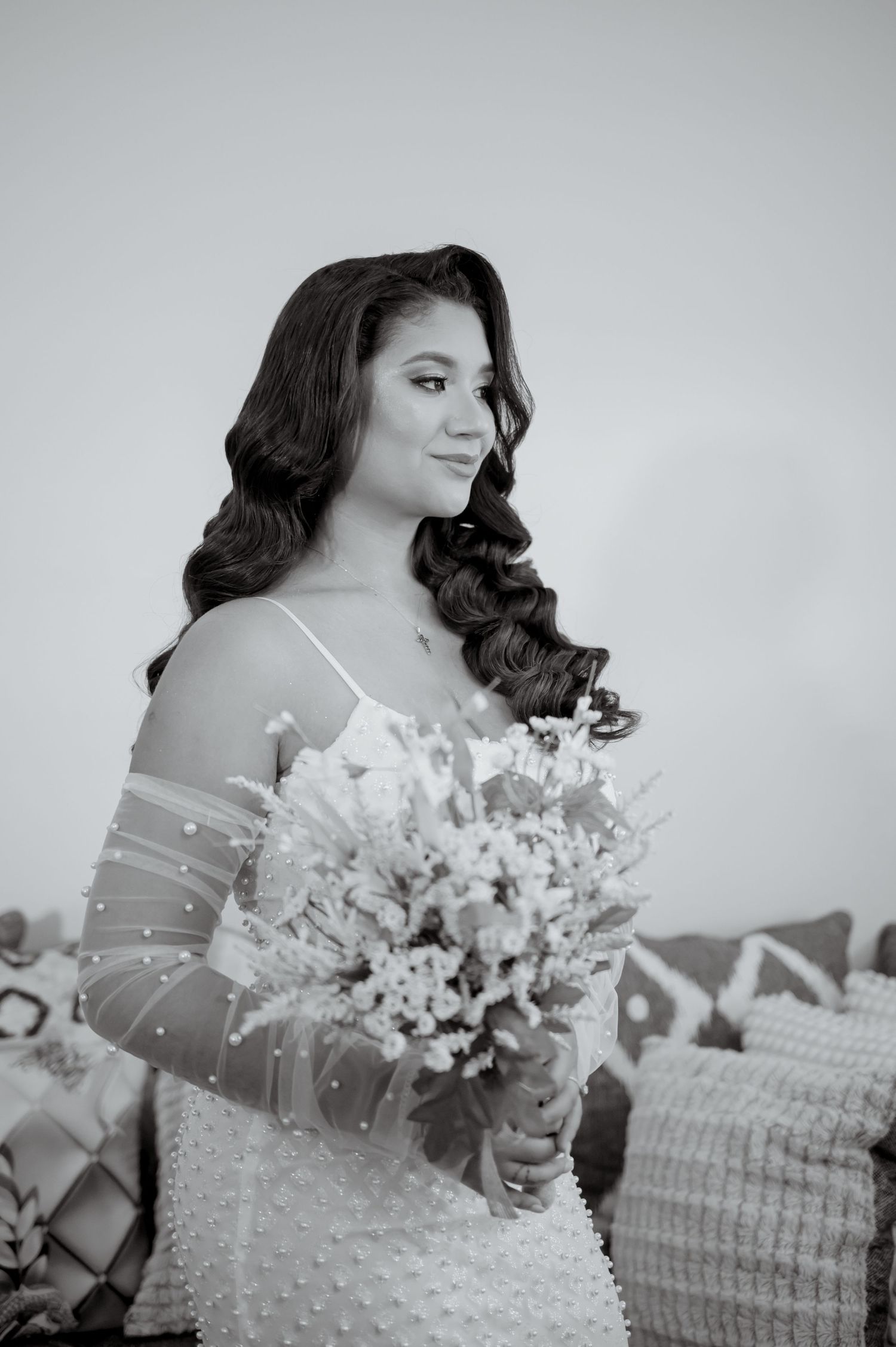 A black and white bridal portrait shows a figure holding a delicate bouquet while wearing an elegant pearl-detailed gown.