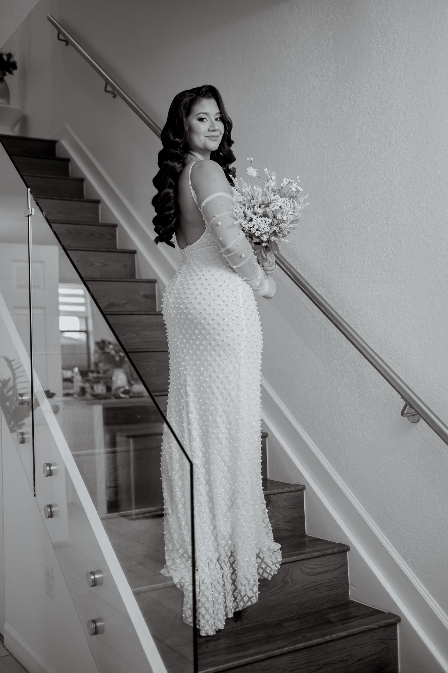 A graceful figure in a dotted white dress stands by a staircase in a series of four black and white photographs.