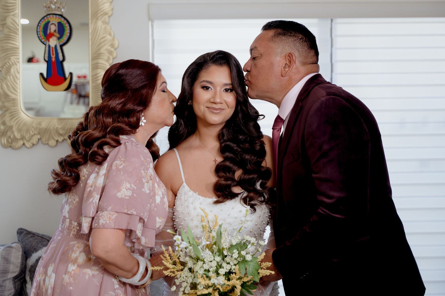A tender family moment at a wedding celebration with burgundy velvet and blush pink attire and a white floral bouquet.
