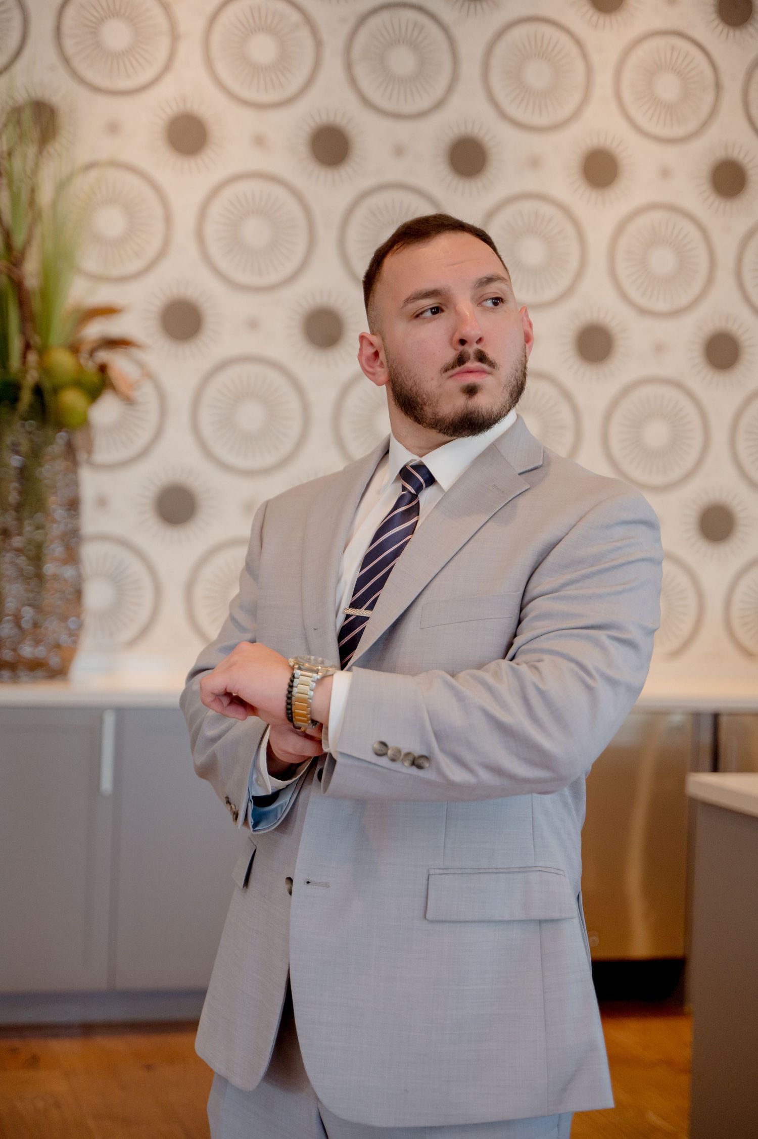 Professional wearing a light gray suit and striped tie poses for a sequence of business headshots against a patterned wall.