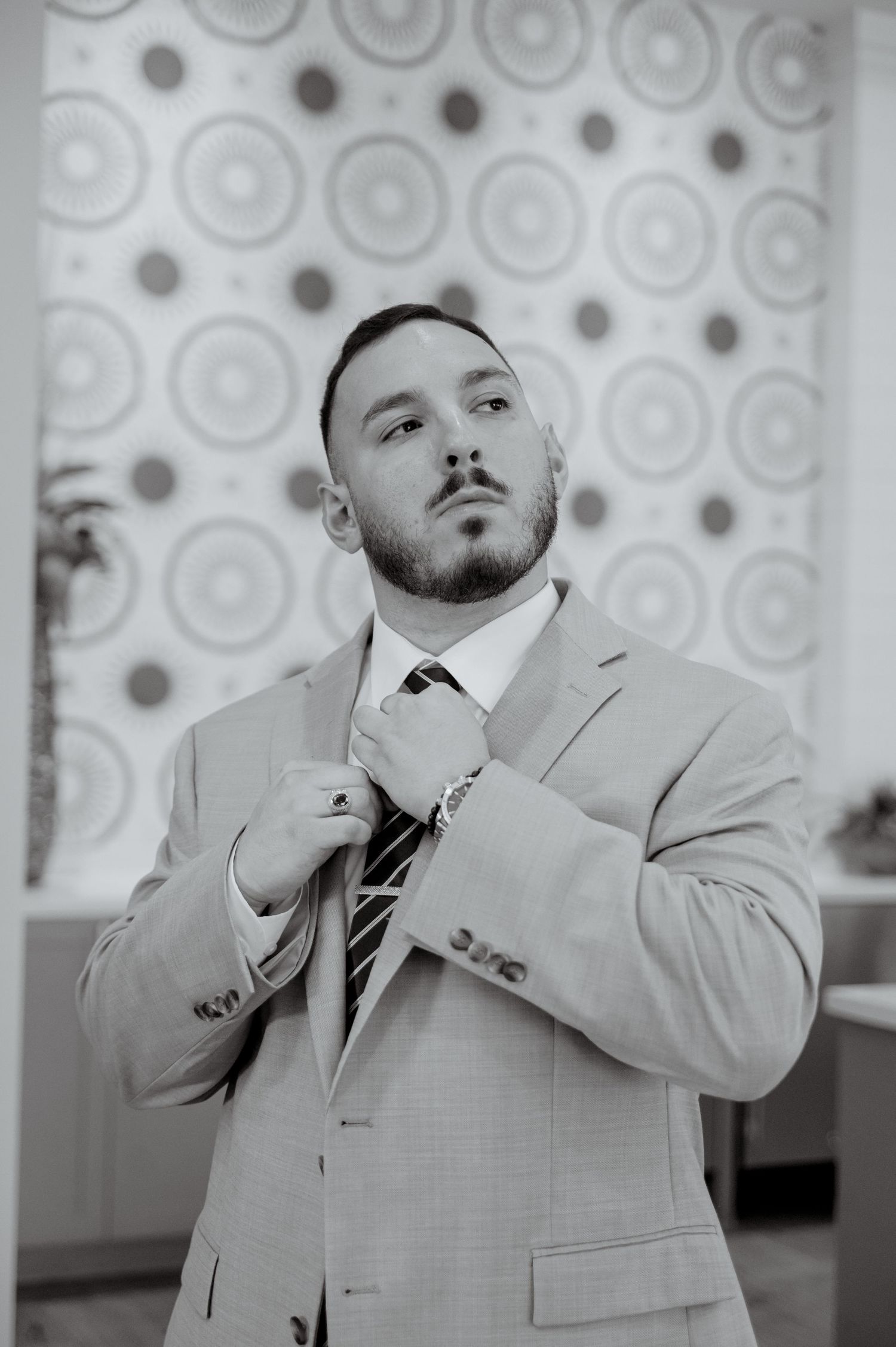 Black and white series of dramatic poses in a light colored suit against a patterned background.