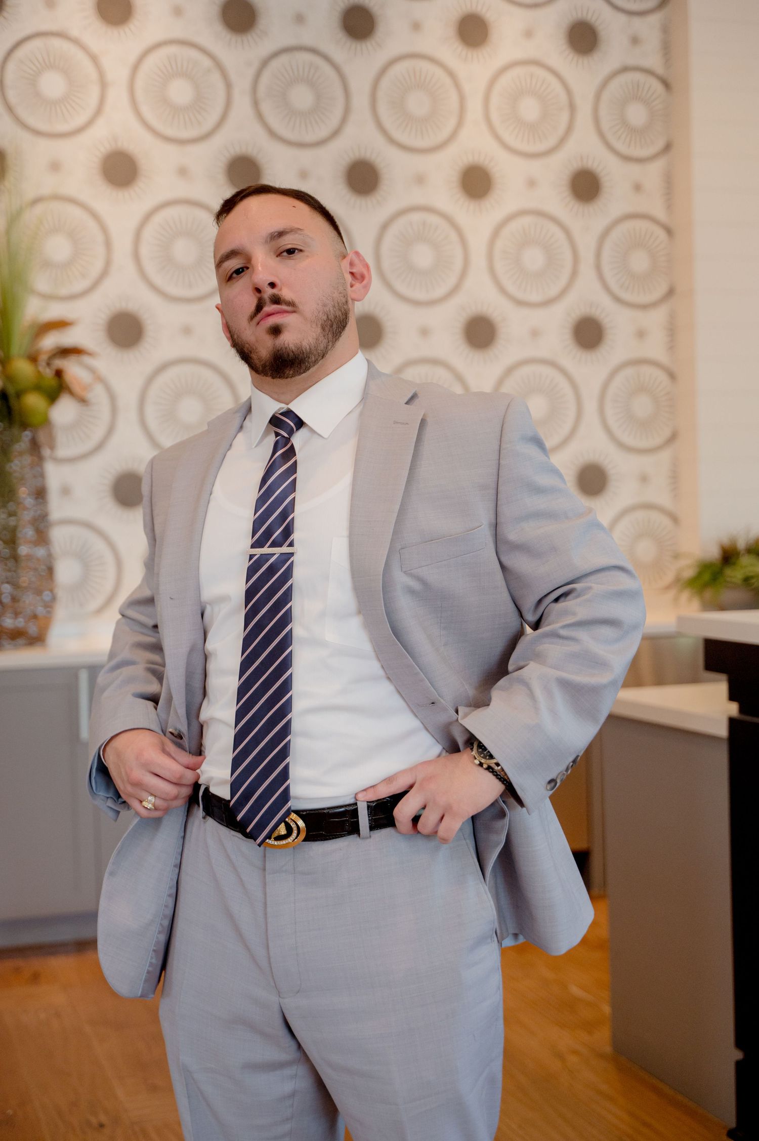 A groom in a light gray suit and striped tie poses in various playful stances against a patterned wall.