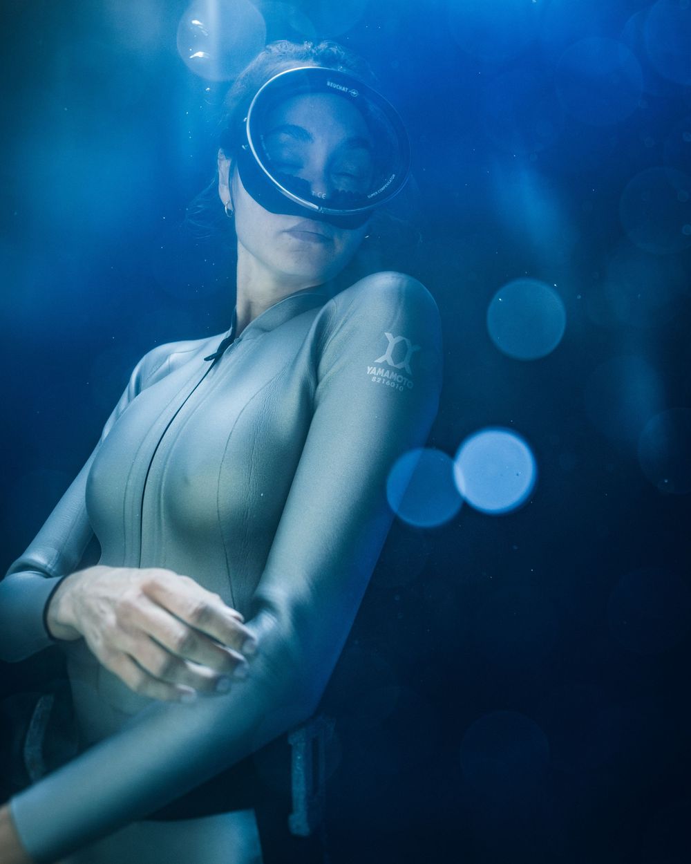 Abstract blue underwater scene with circular bokeh lights and ethereal silhouettes creating a dreamy aquatic atmosphere.