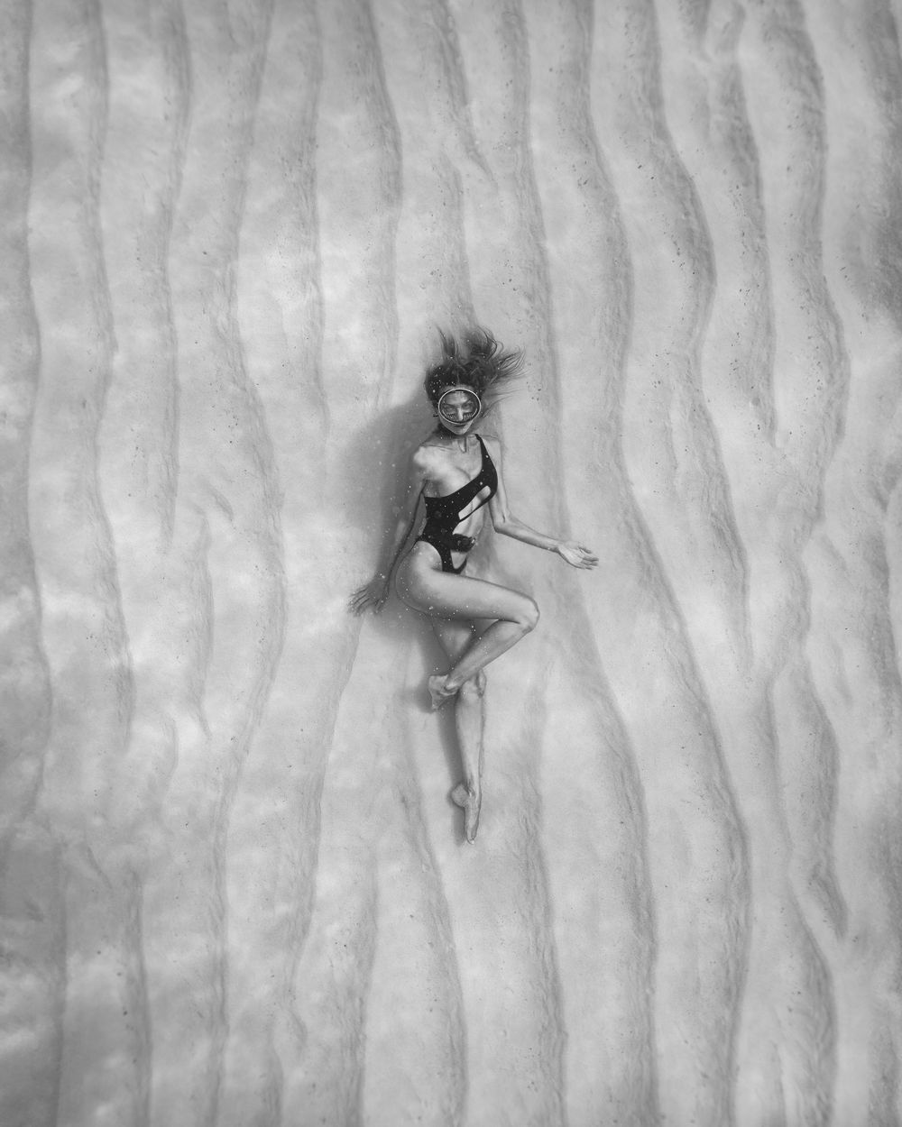 Five black and white artistic photographs show a person gracefully lying in different poses against a textured wall.
