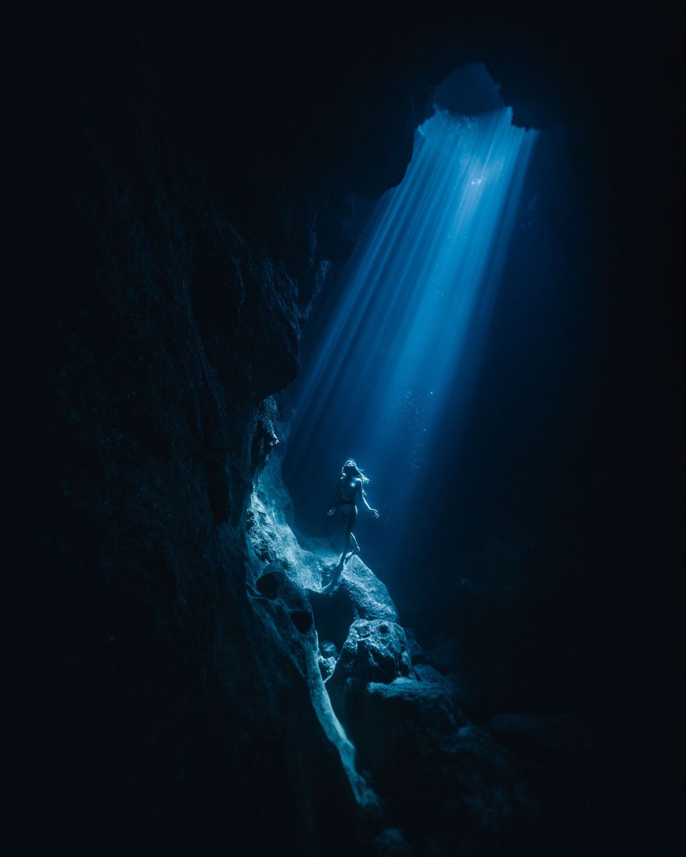 Ethereal blue light beams illuminate a mystical underwater cave creating dramatic shadows and reflections.