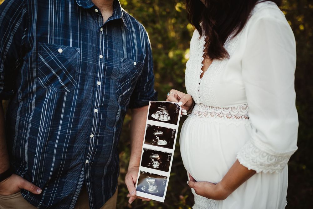 Couple holds ultrasound photos during outdoor golden hour maternity photography session wearing navy and white.