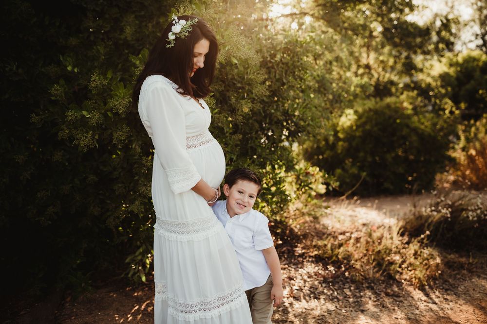 An expectant couple poses in a sunlit forest setting during a golden hour maternity photoshoot.