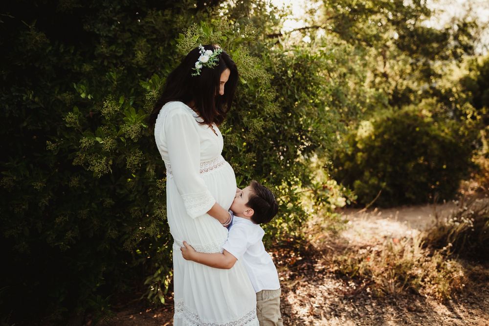Romantic couple in white outfits embrace during golden hour photoshoot in a sunlit forest setting with glowing backlight.