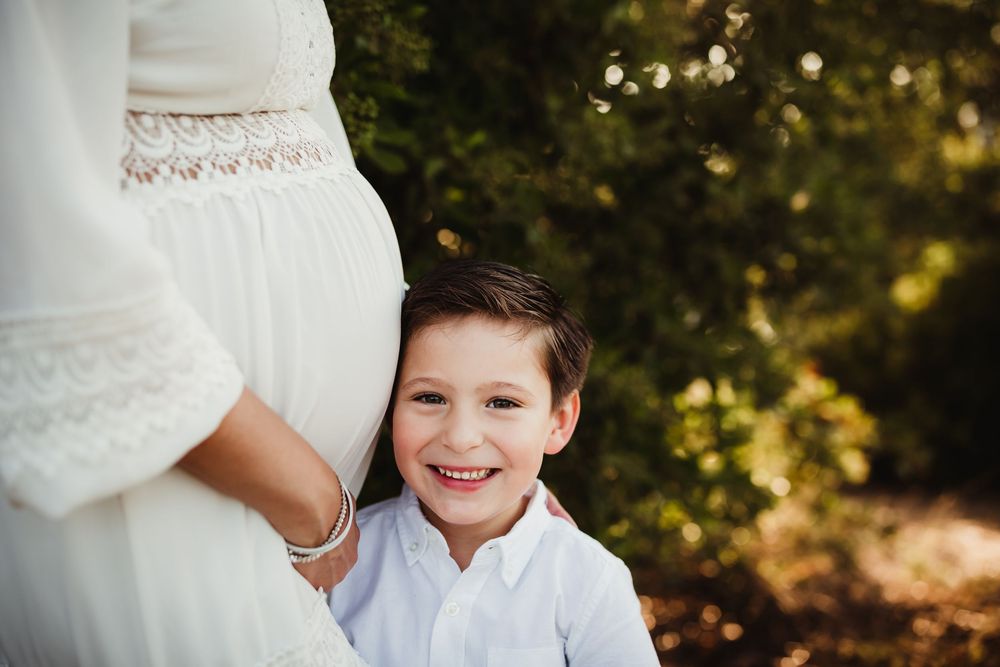 A family poses together in a golden-lit outdoor setting wearing coordinated white and cream colored outfits.