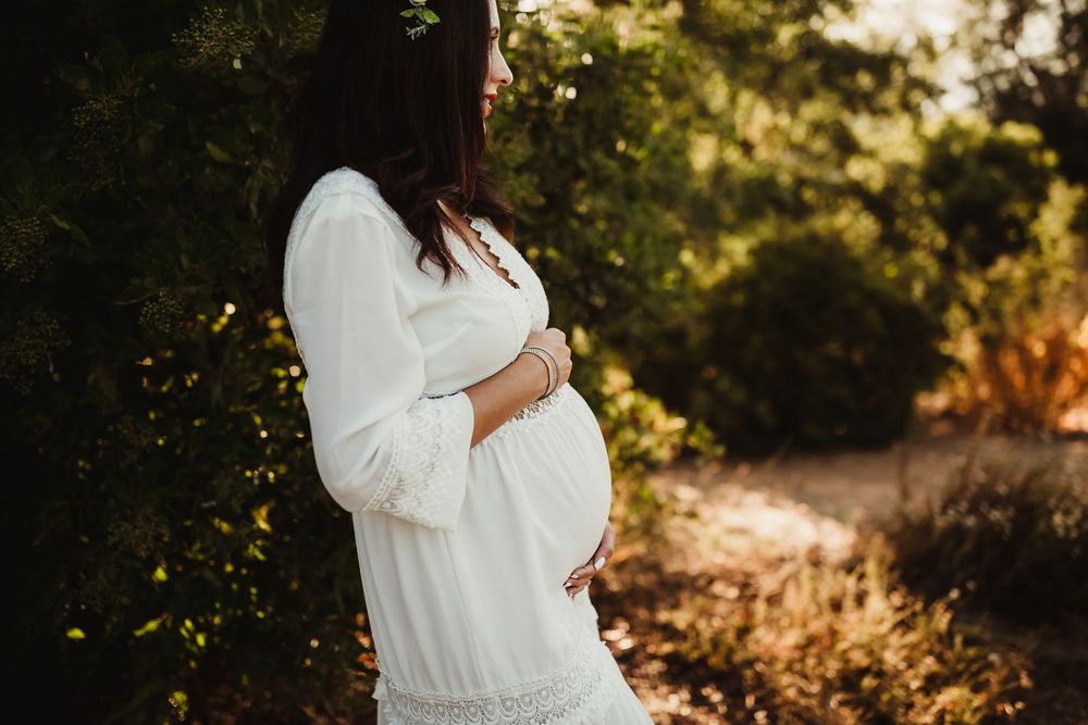 Maternity portrait series in golden sunlight with couple displaying ultrasound photos in white dress and plaid shirt.