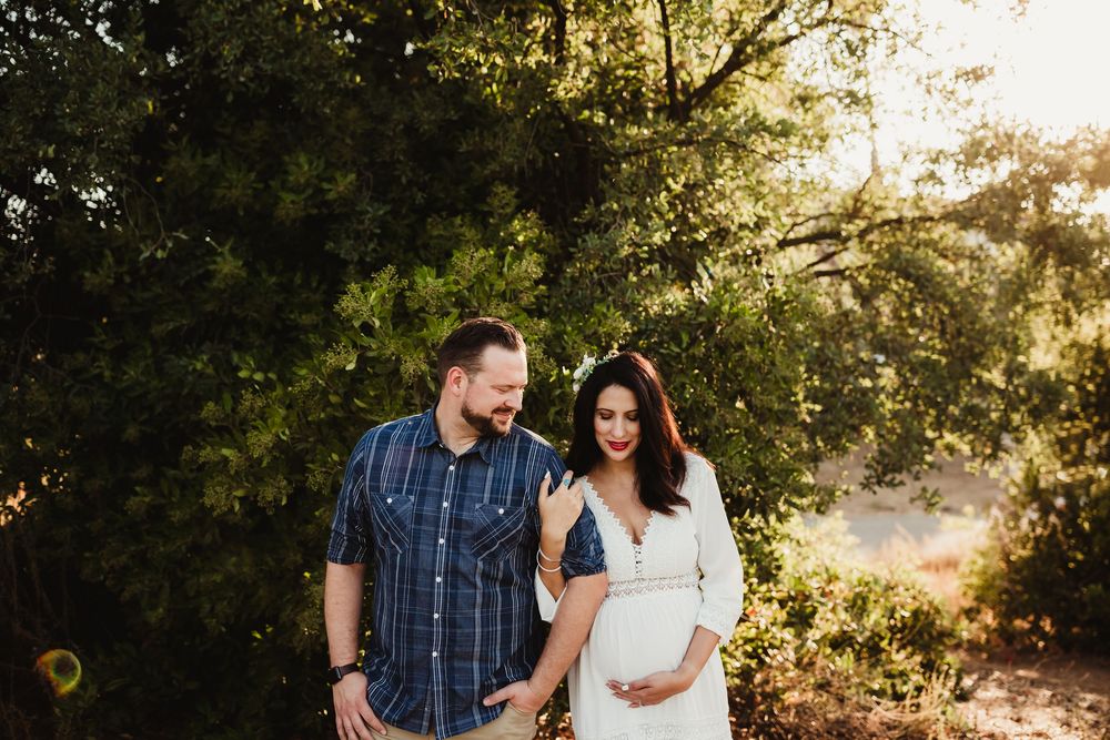 A couple shares intimate moments during a golden hour photoshoot in a sun-dappled meadow.
