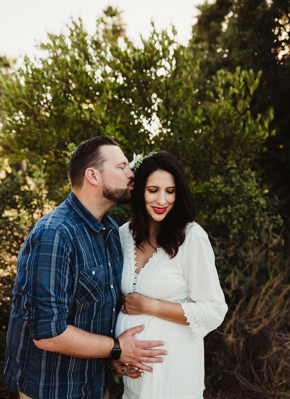 A couple shares an intimate moment outdoors while wearing white dress and plaid shirt.