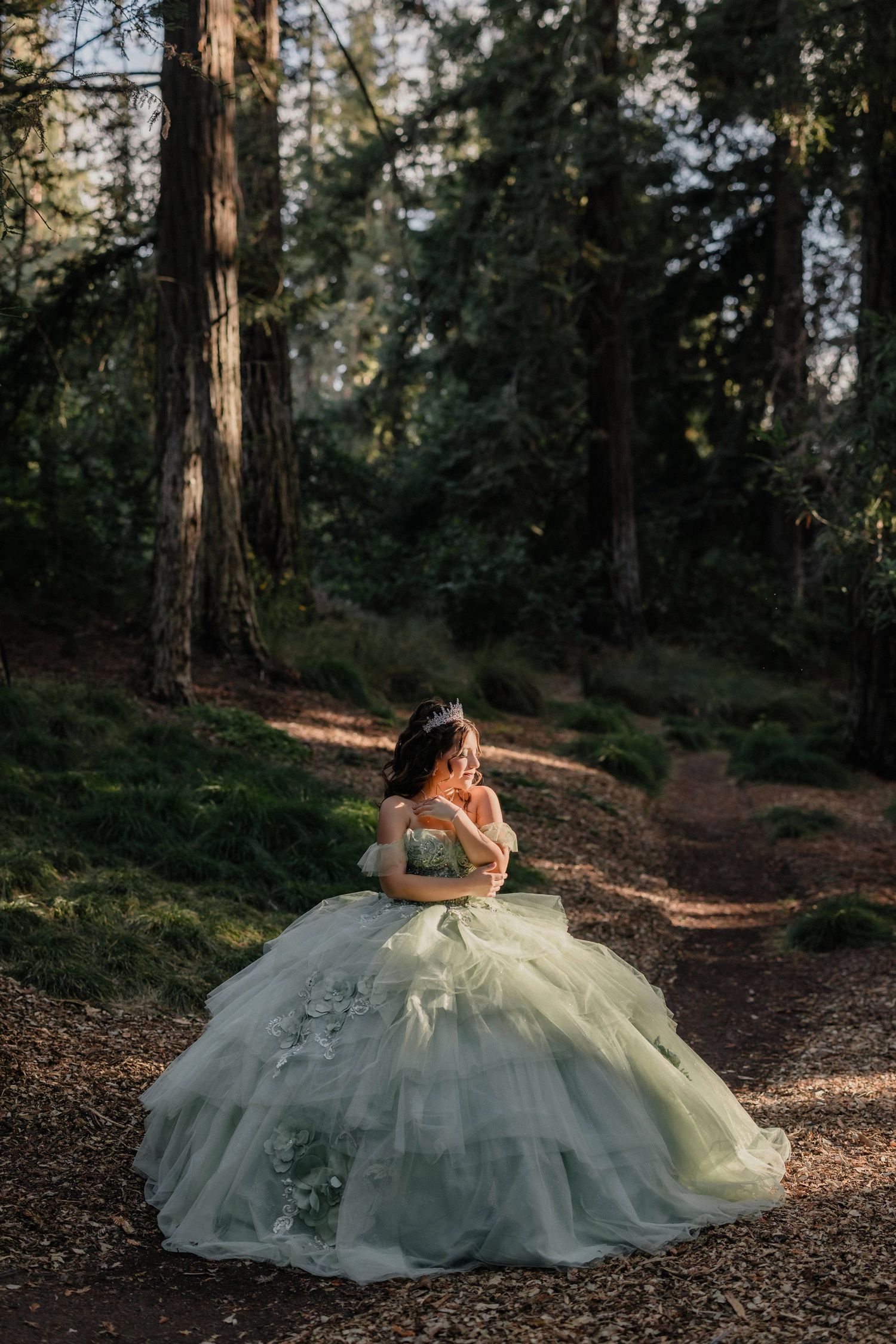 An elegant mint green ballgown cascades across forest floor amidst redwood trees and filtered afternoon light.