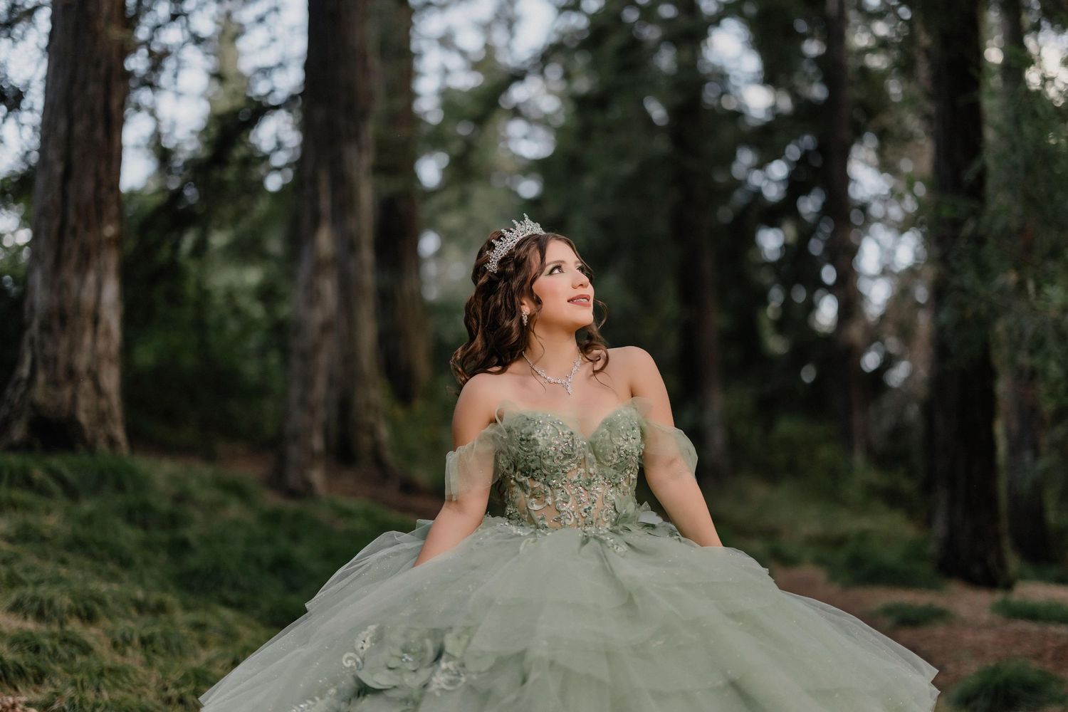 A stunning sage green ball gown with intricate details photographed in a misty forest setting.