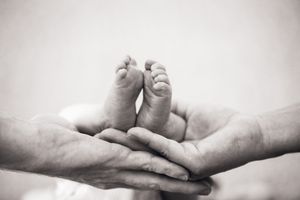 Black and white photo of a newborn baby's tiny feet cradled gently in adult hands.