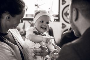 A baby wearing a cap smiles brightly in a black and white photograph while being held.