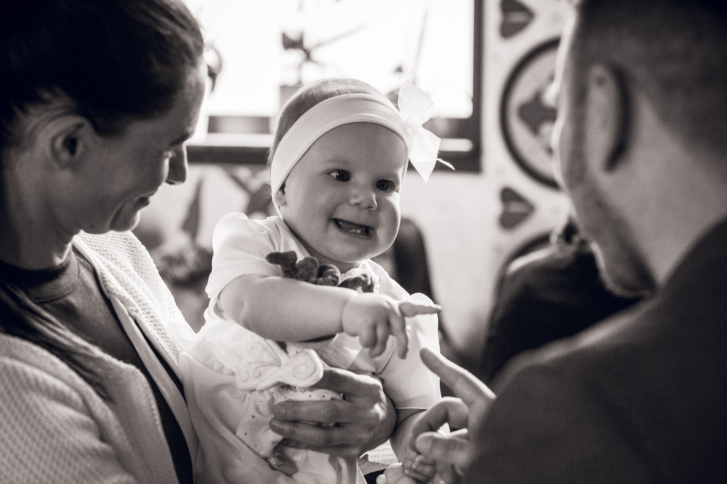 A baby wearing a cap smiles brightly in a black and white photograph while being held.