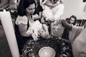Black and white photo of a woman holding a baby over a baptismal font during a christening ceremony in a church.