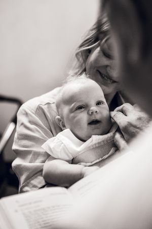 Black and white photo of a smiling mother tenderly holding her newborn baby, who gazes upward curiously.