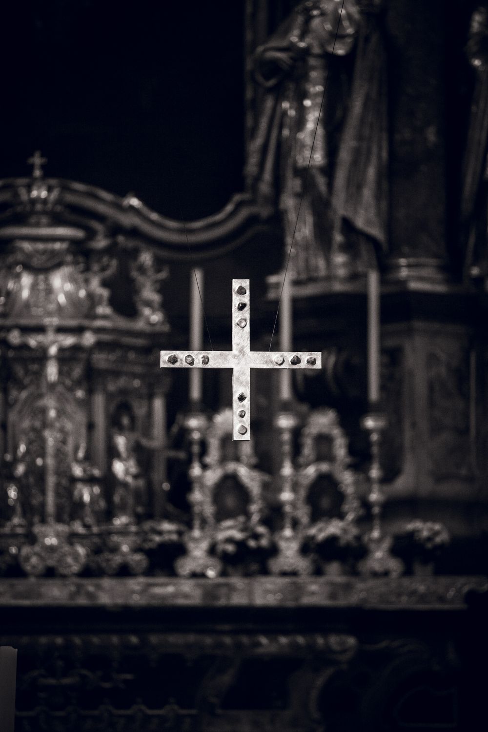 Black and white photo of an ornate Christian cross in focus against a blurred church altar background.
