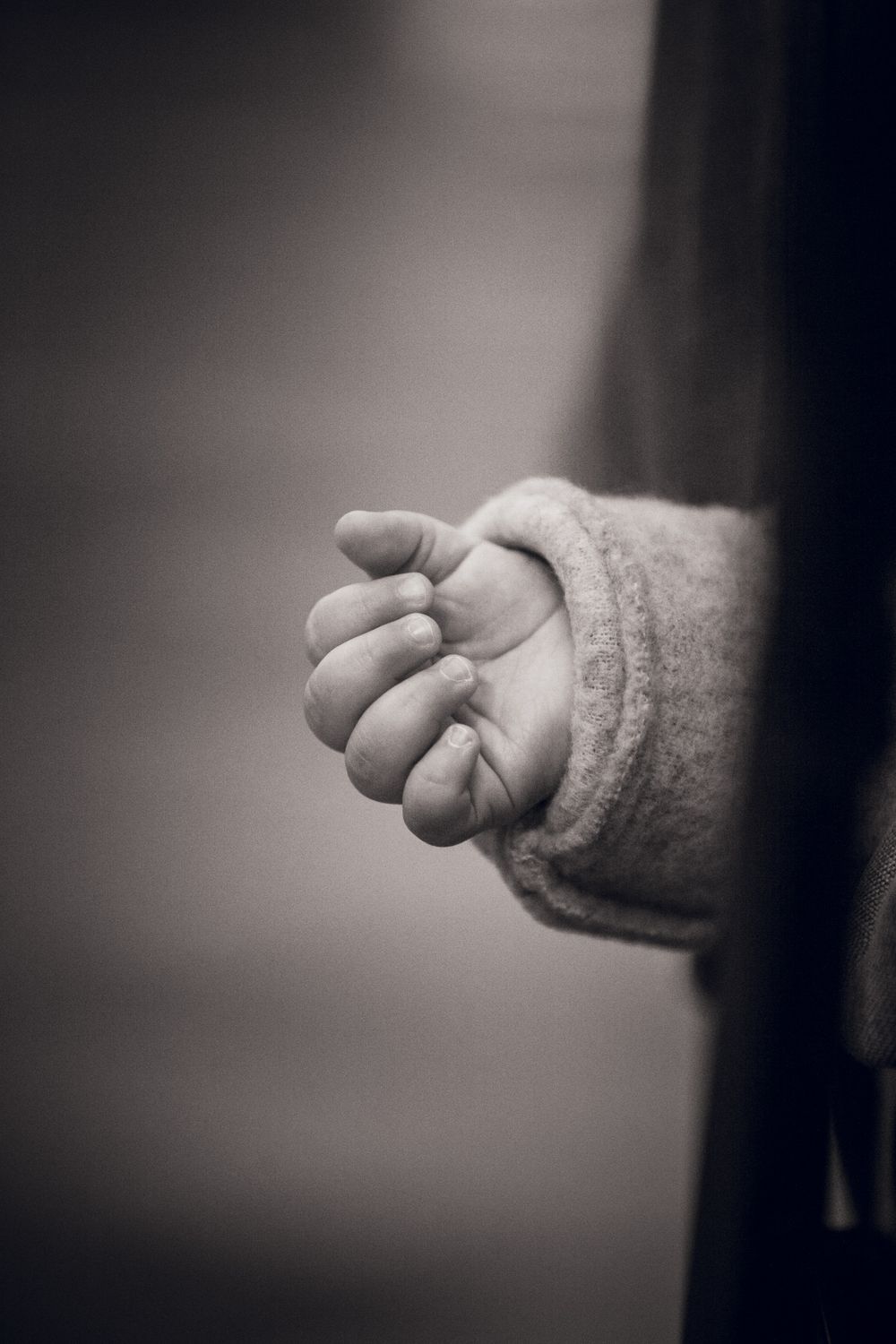 Black and white close-up of a small child's hand gently clasped, wearing a soft knit sweater sleeve.