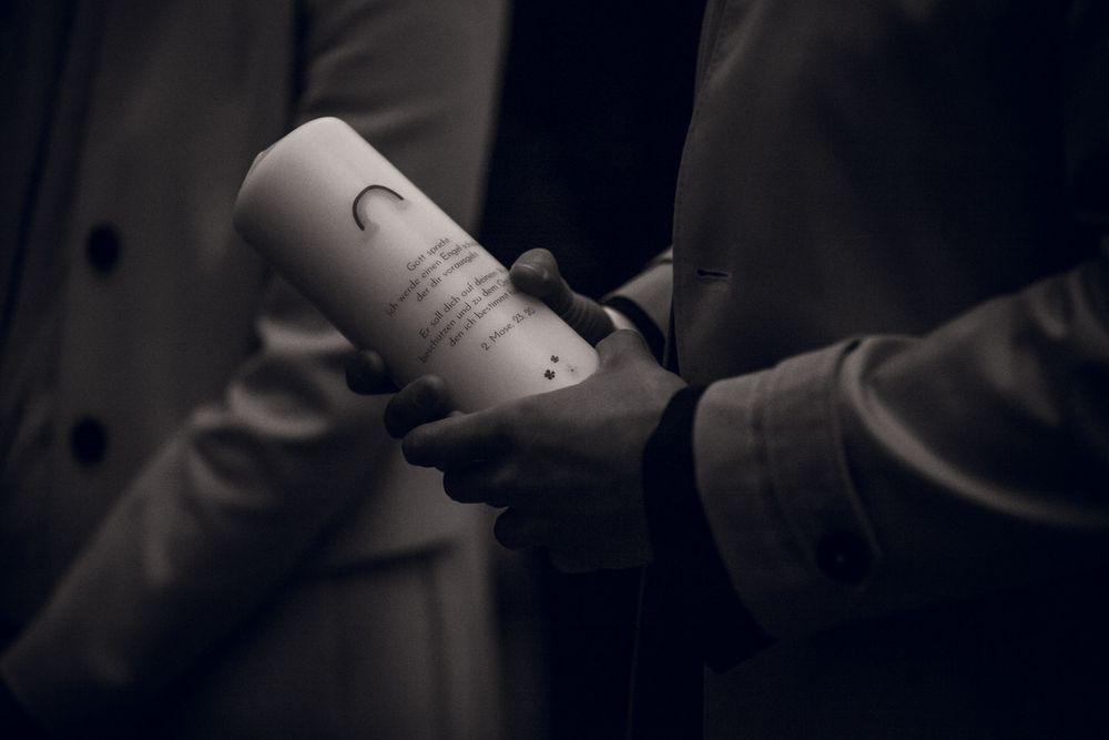 Person holding a white cylindrical candle with text in a dark, moody black and white photograph.