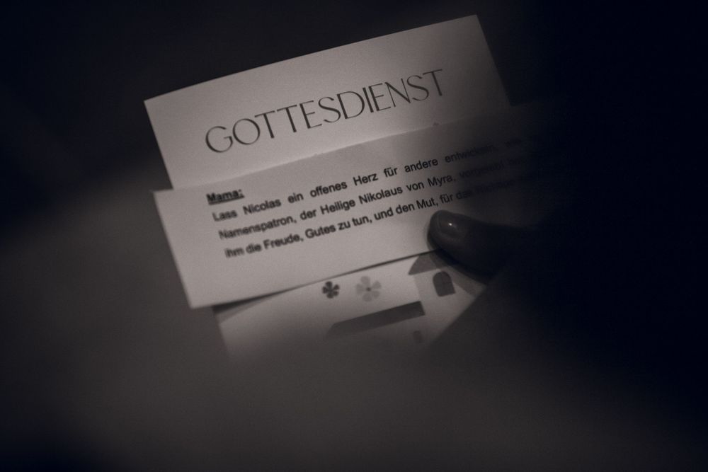 A dimly lit card reading GOTTESDIENST with German text, photographed in moody black and white lighting.