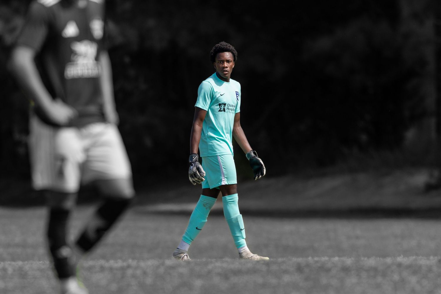 Player in teal uniform stands ready on sports field.