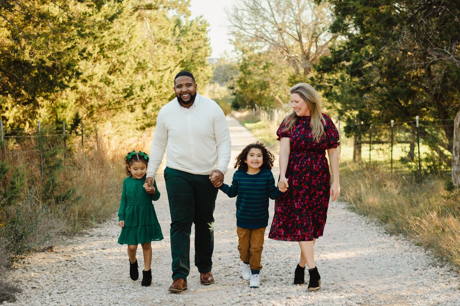 A happy family of four holds hands while walking down a nature path together.