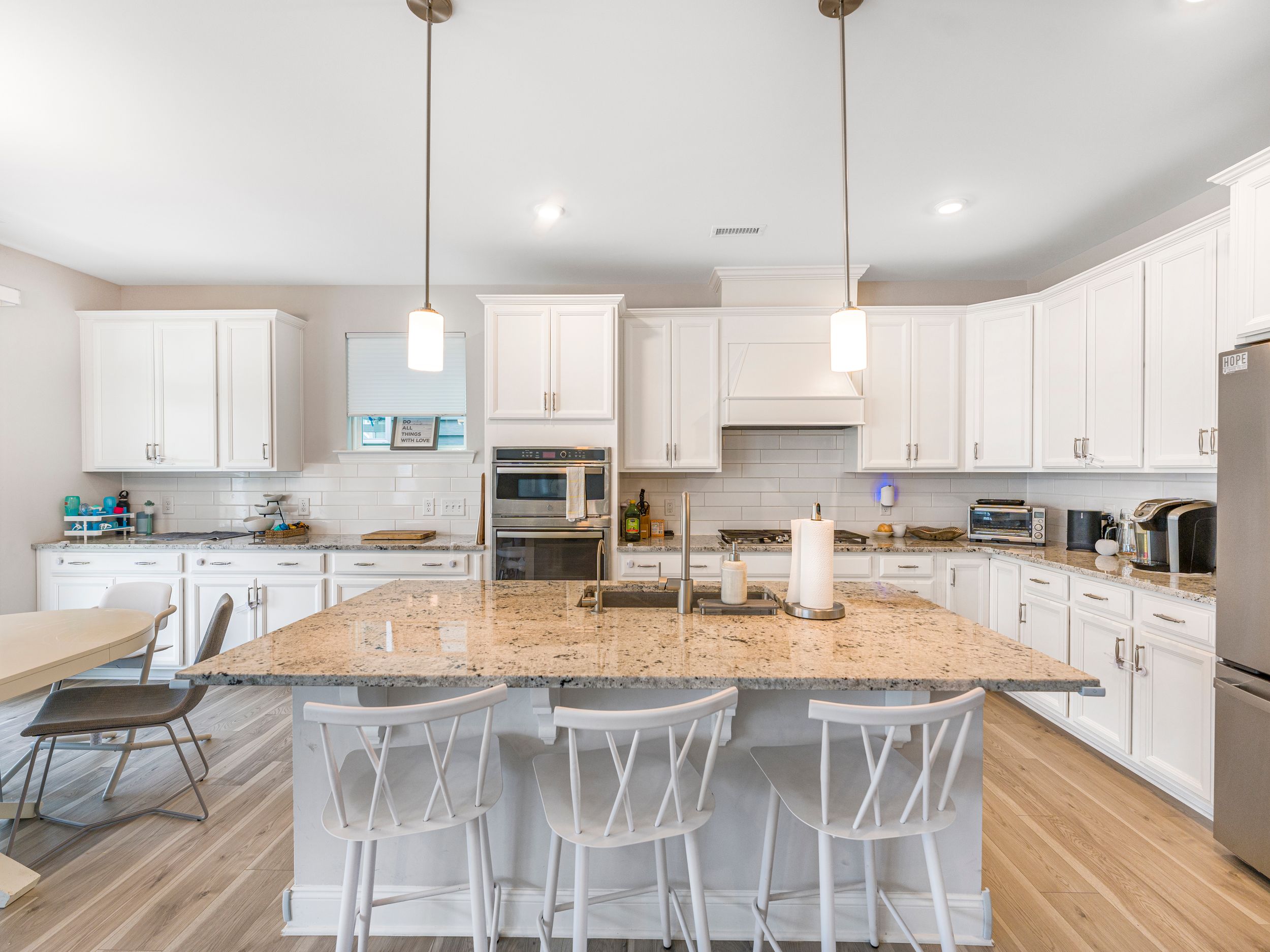 Modern white kitchen with granite countertops, pendant lights and wood flooring.