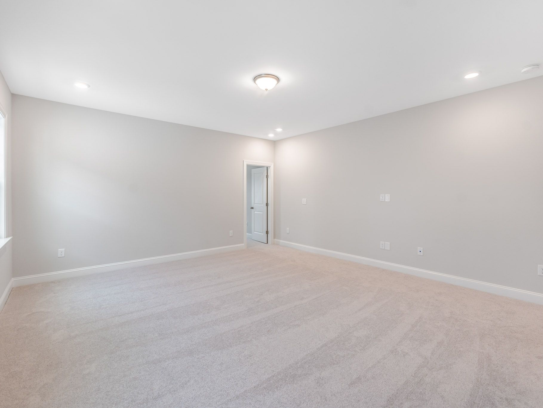 Spacious empty room with gray walls, recessed lighting, and light-colored carpeting.