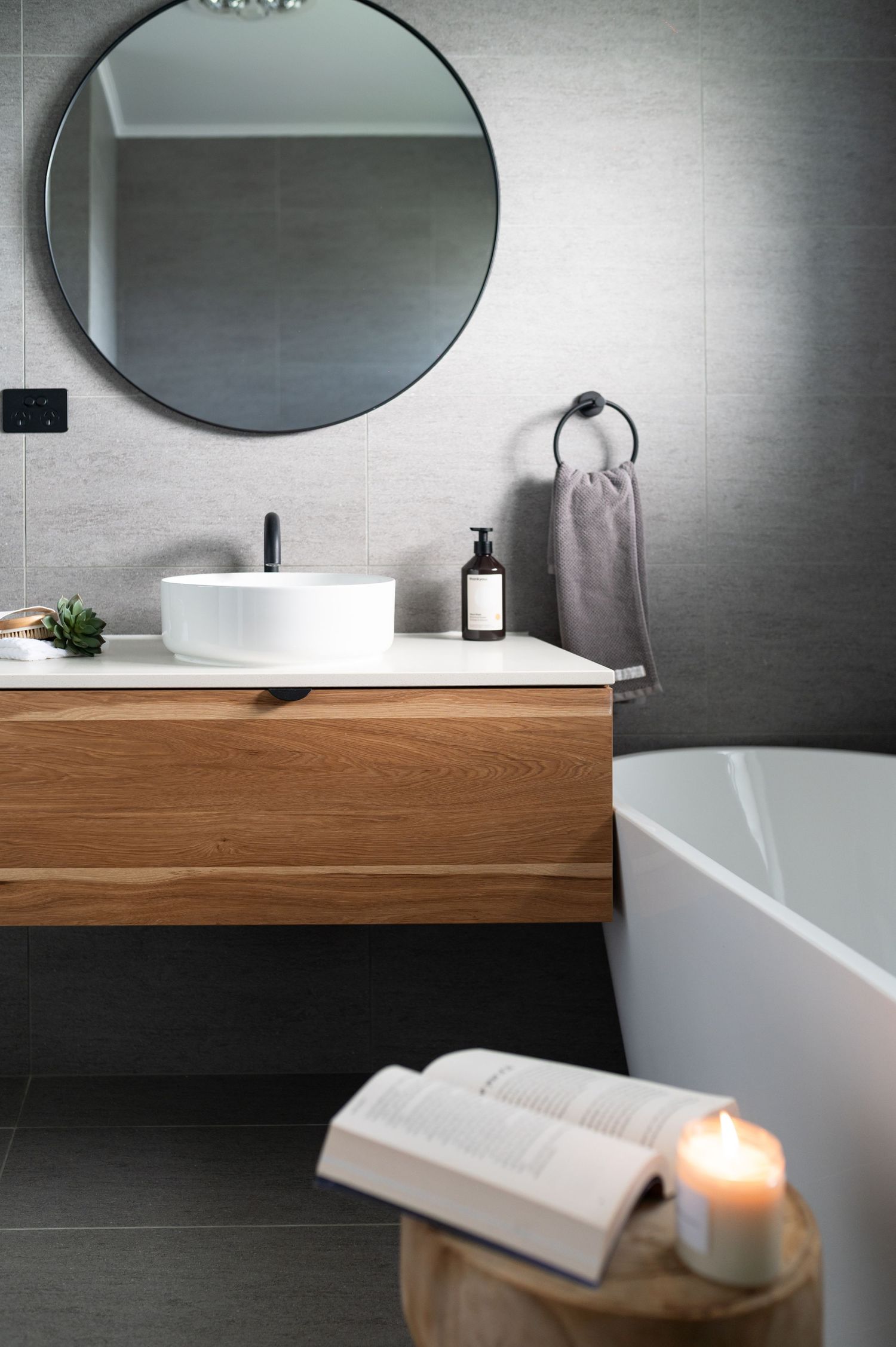 Contemporary bathroom vanity with wooden countertop, round mirror, and soft candlelight creates a serene spa-like atmosphere.