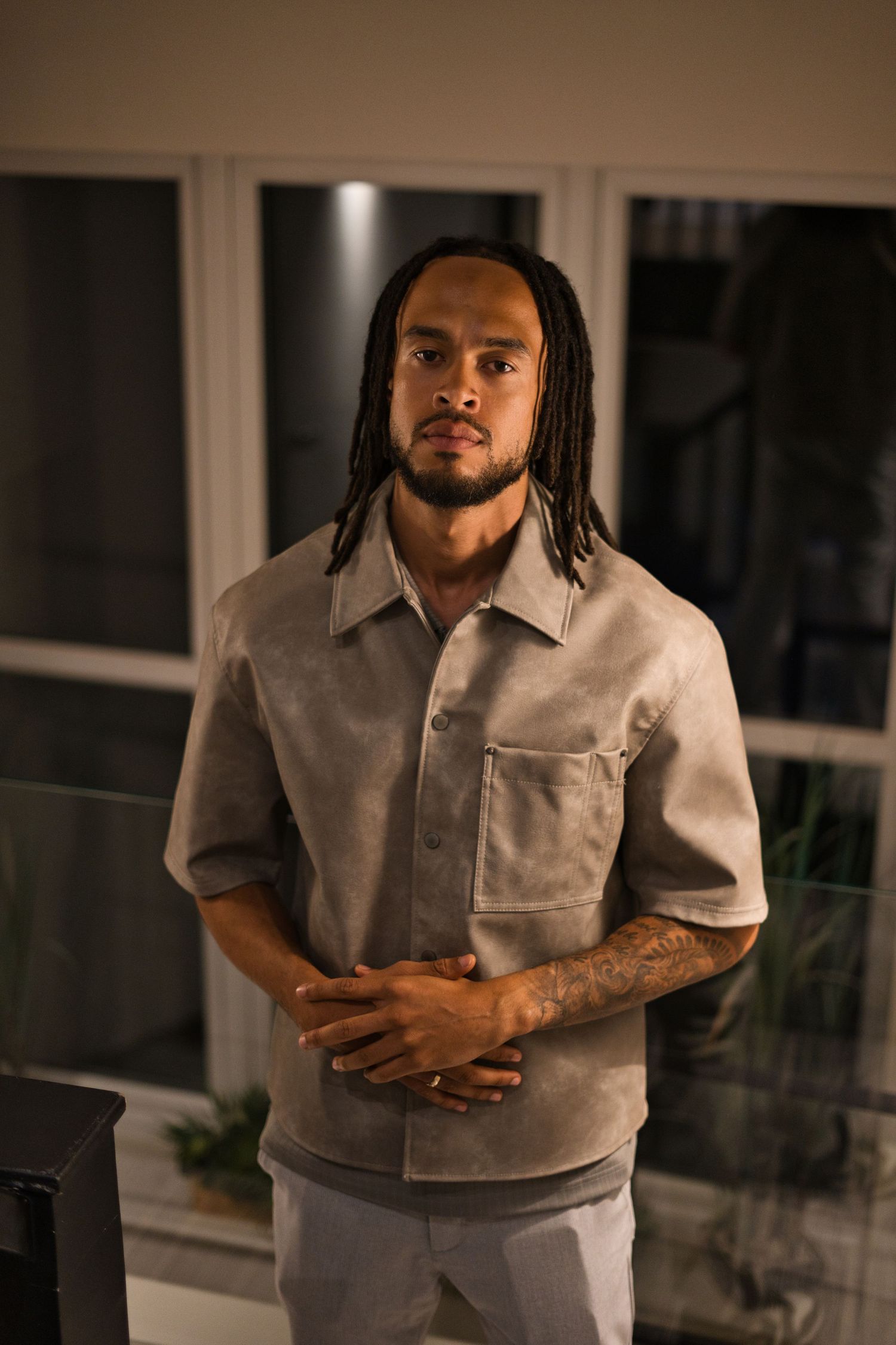 A person in a gray collared shirt poses against a dark background in a studio-like setting.