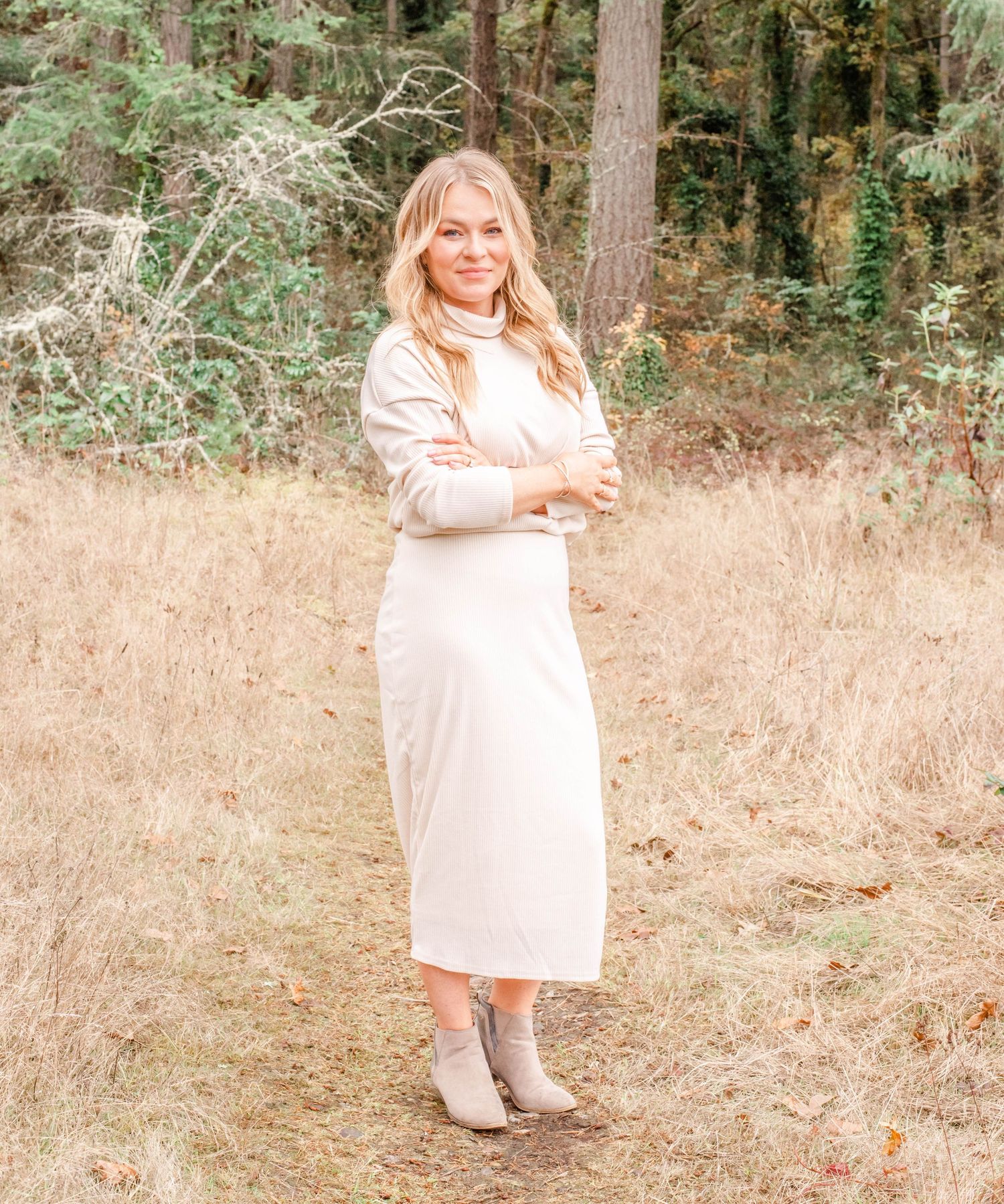 Someone posing playfully in a light beige dress against a wooded outdoor backdrop.