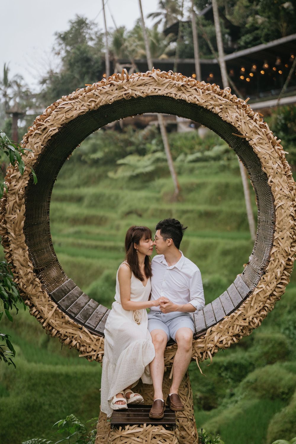 A couple sharing an intimate moment on a decorative circular nest swing in a tropical setting.