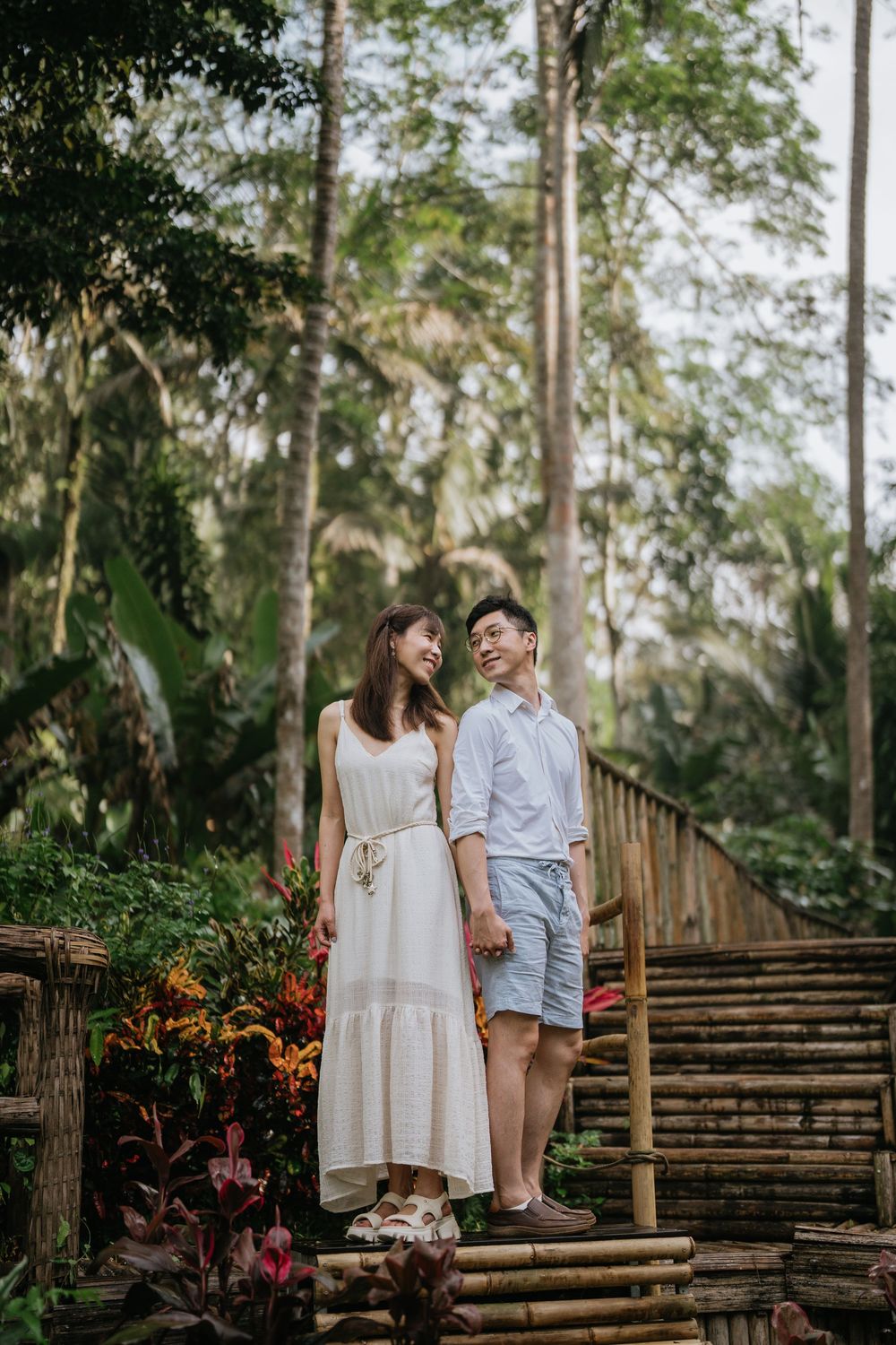 A romantic photoshoot on wooden steps surrounded by tropical plants and tall trees.