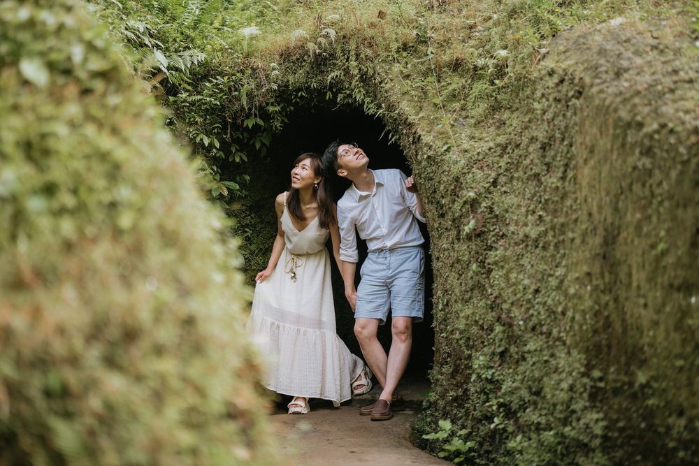 A couple poses together against a backdrop of lush green foliage in a garden setting.