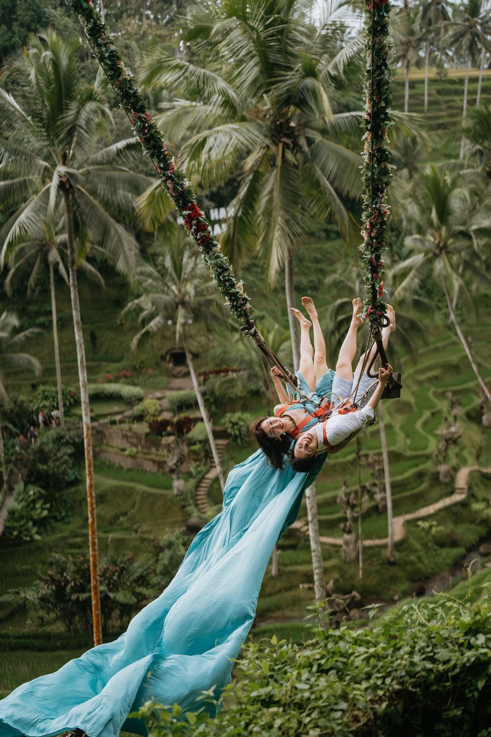 A person in a flowing turquoise dress swings dramatically against a backdrop of tropical palm trees.