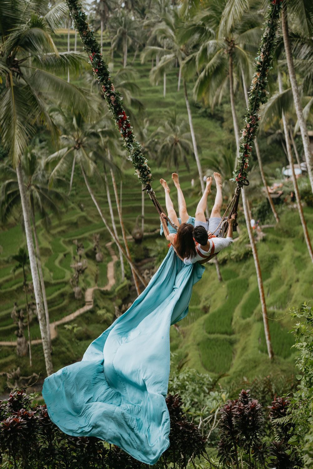 A flowing turquoise dress creates movement as someone swings in a palm tree grove.
