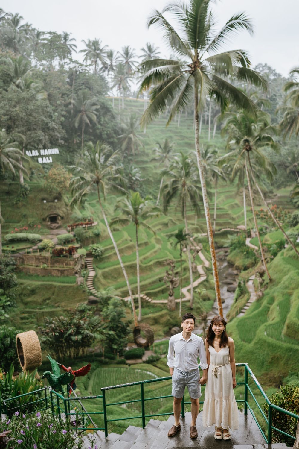 A couple walks through the famous Tegalalang rice terraces in Bali surrounded by palm trees.