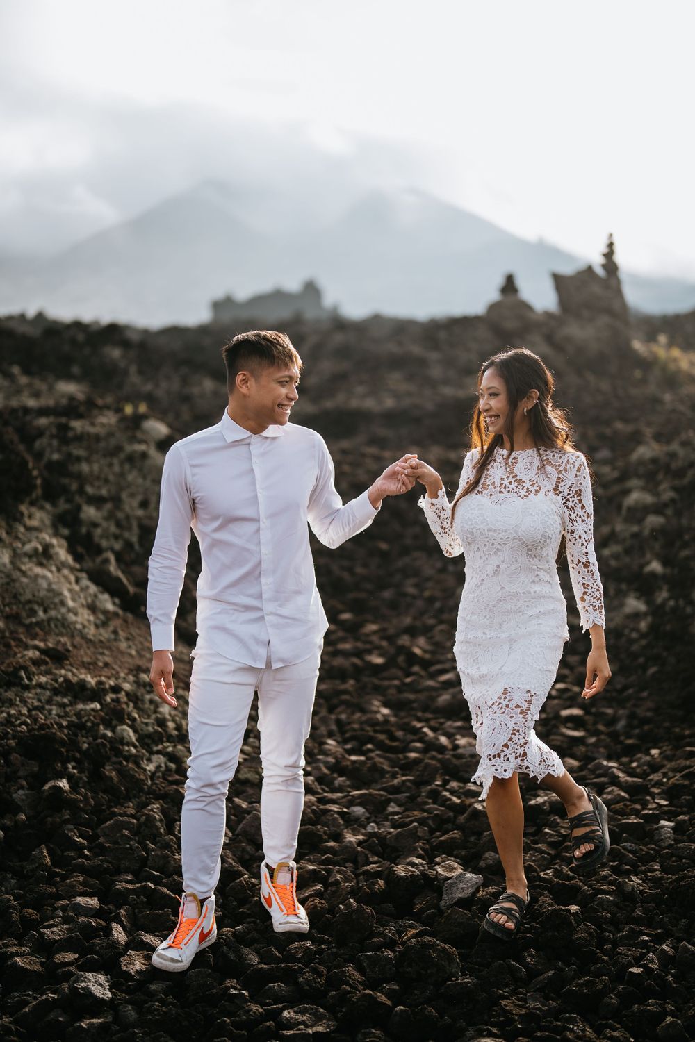 Couple carefully traversing rocky volcanic landscape while holding hands.