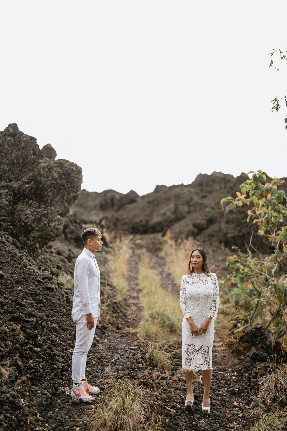 Two people in white outfits standing among volcanic rocks and grass.